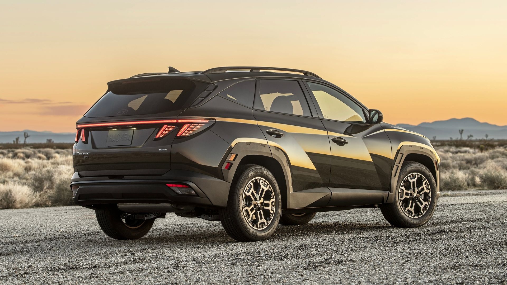 Vue 3/4 arrière sur le Hyundai Tucson Hybride 2025 au couché du soleil.